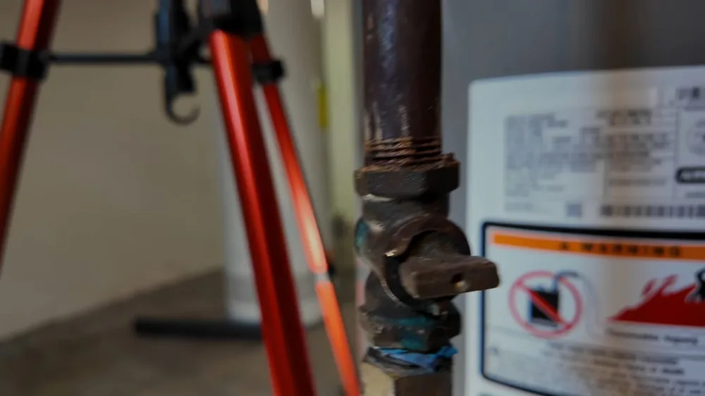 Gas shutoff valve on a pipe beside a water heater, with red tripod legs and the heater's warning label in view