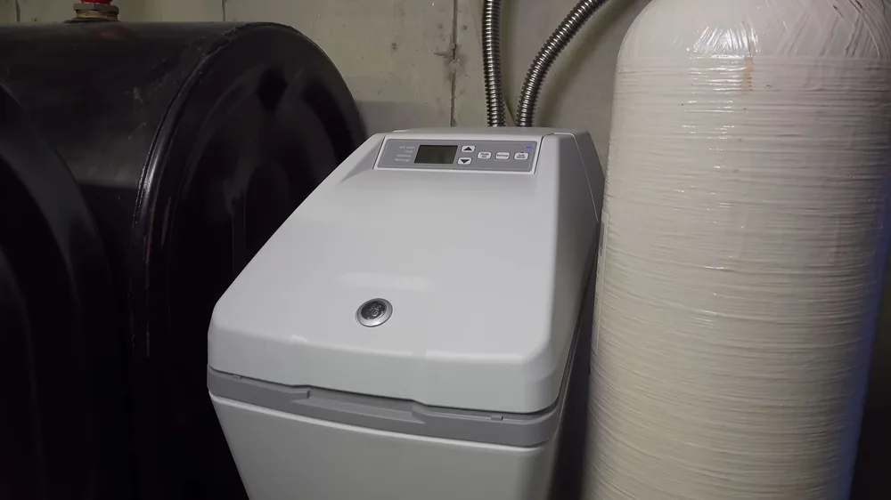 Light gray water softener cabinet standing beside a white mineral tank in a garage corner