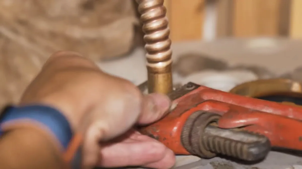 Hand gripping a corrugated copper connector with a red pipe wrench