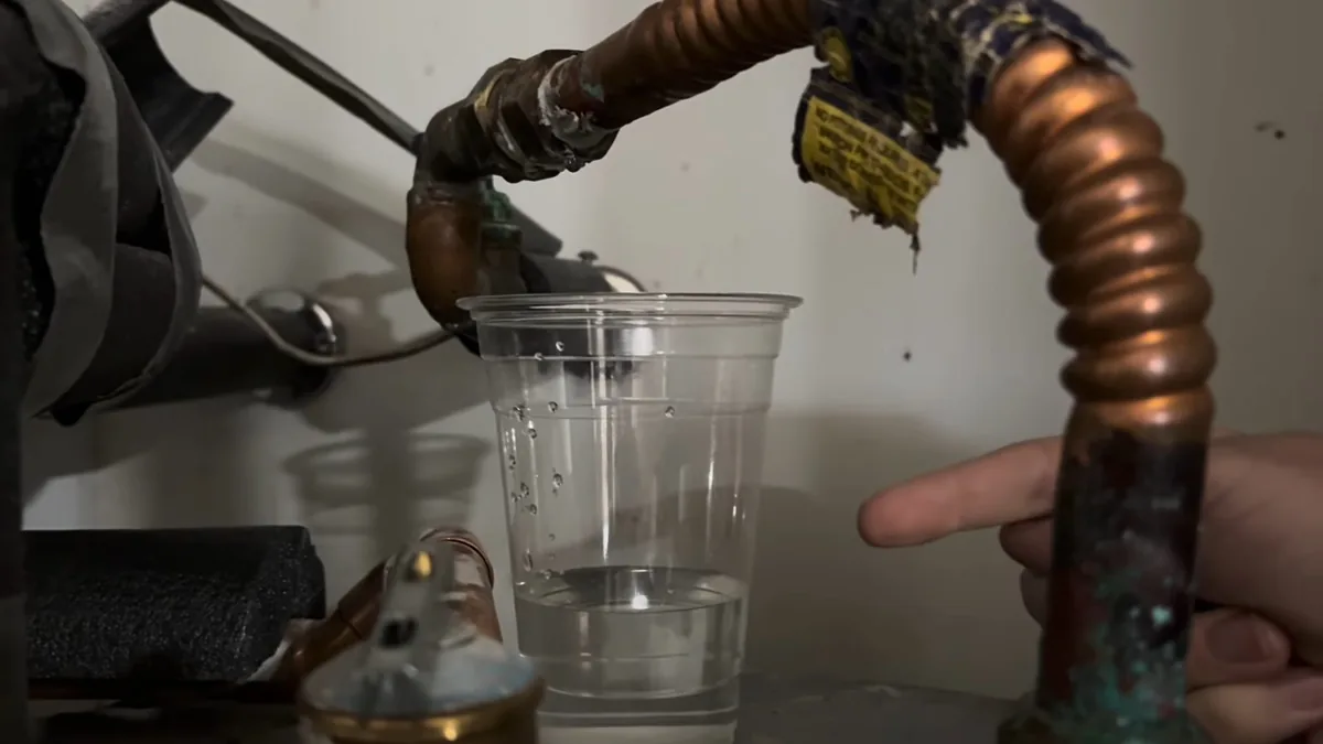 Hand holding a wrench on a corrugated copper connector above a clear cup that is catching drips