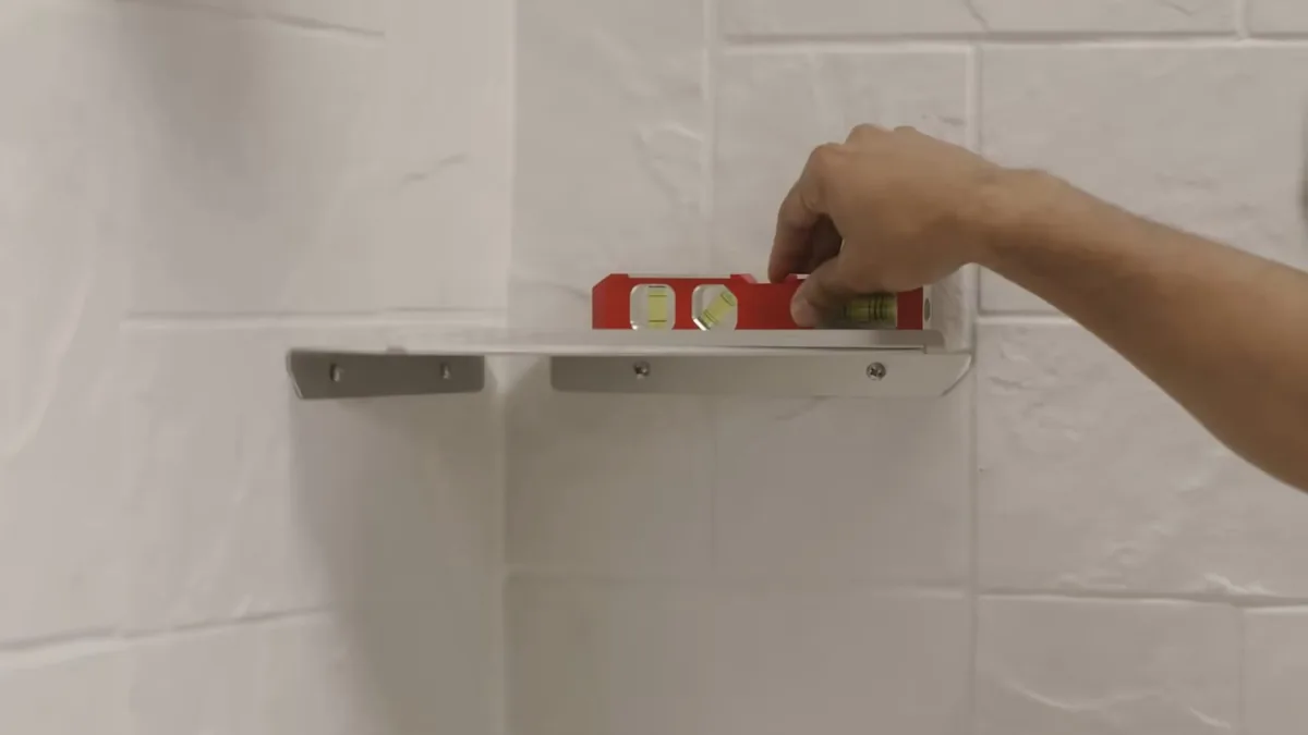 Hand placing a small level on a metal shelf bracket against white tile
