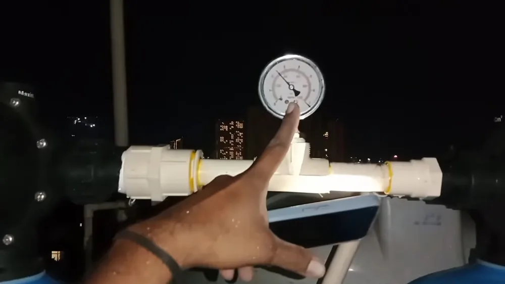 Hand pointing at a round pressure gauge mounted on a short white pipe section at night