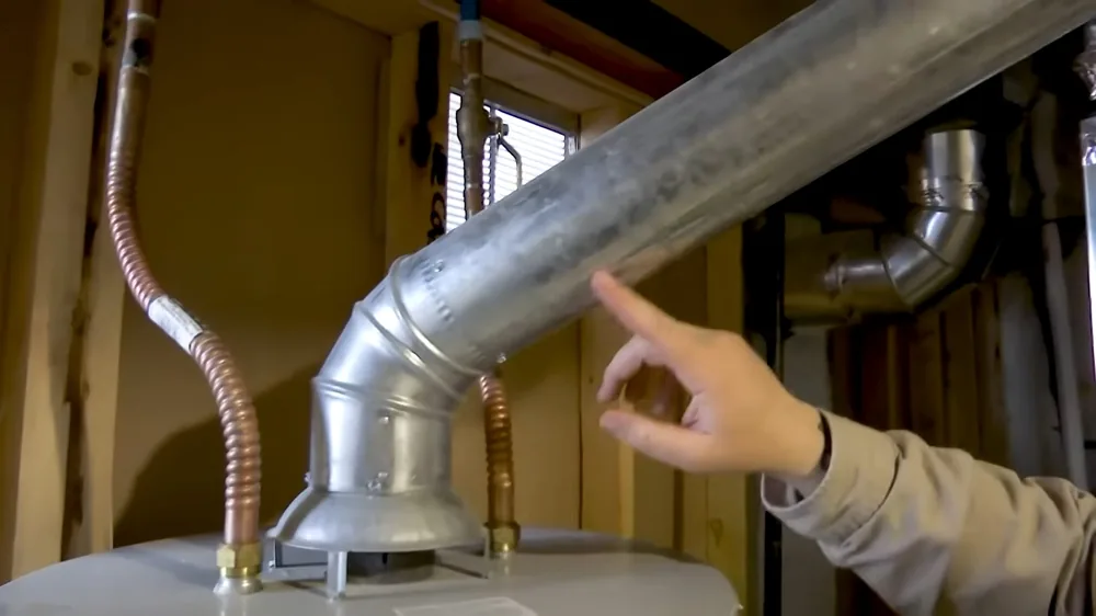 Hand pointing to a metal vent pipe rising from the top of a water heater