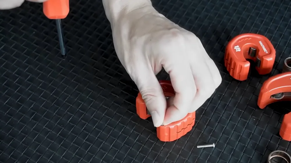 Hand pressing red pipe cutter pieces into place on a black mat
