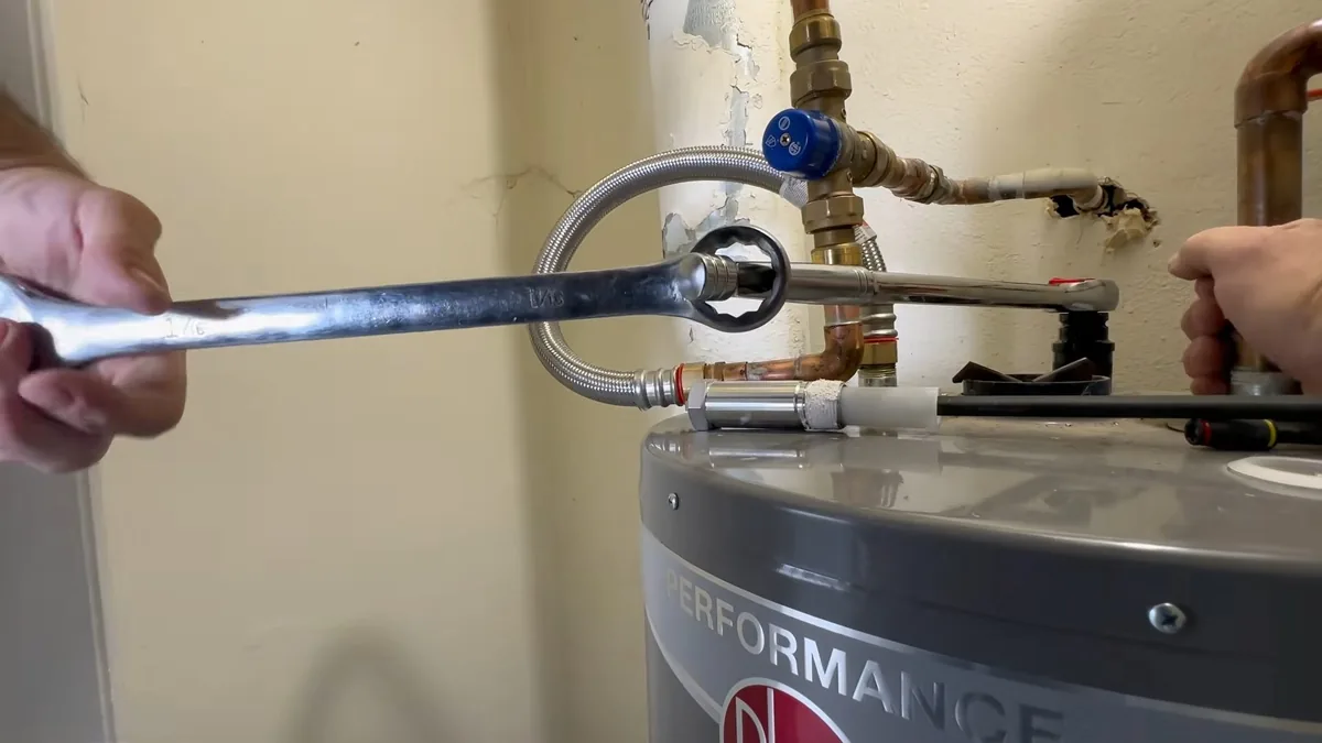 Hand tightening a flexible line at the top of a tank water heater with a wrench, a blue valve beside it