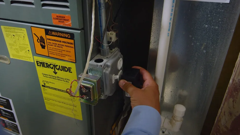 Hand turning the gas control on a water heater, with yellow energy guide labels beside it