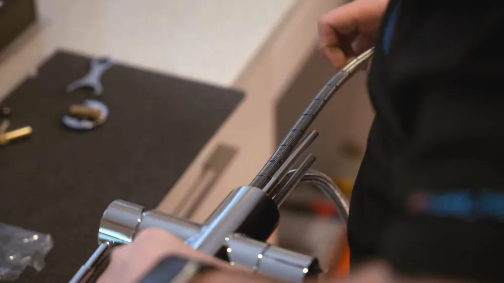 Hands assembling a chrome faucet with a braided hose on a countertop beside a wrench