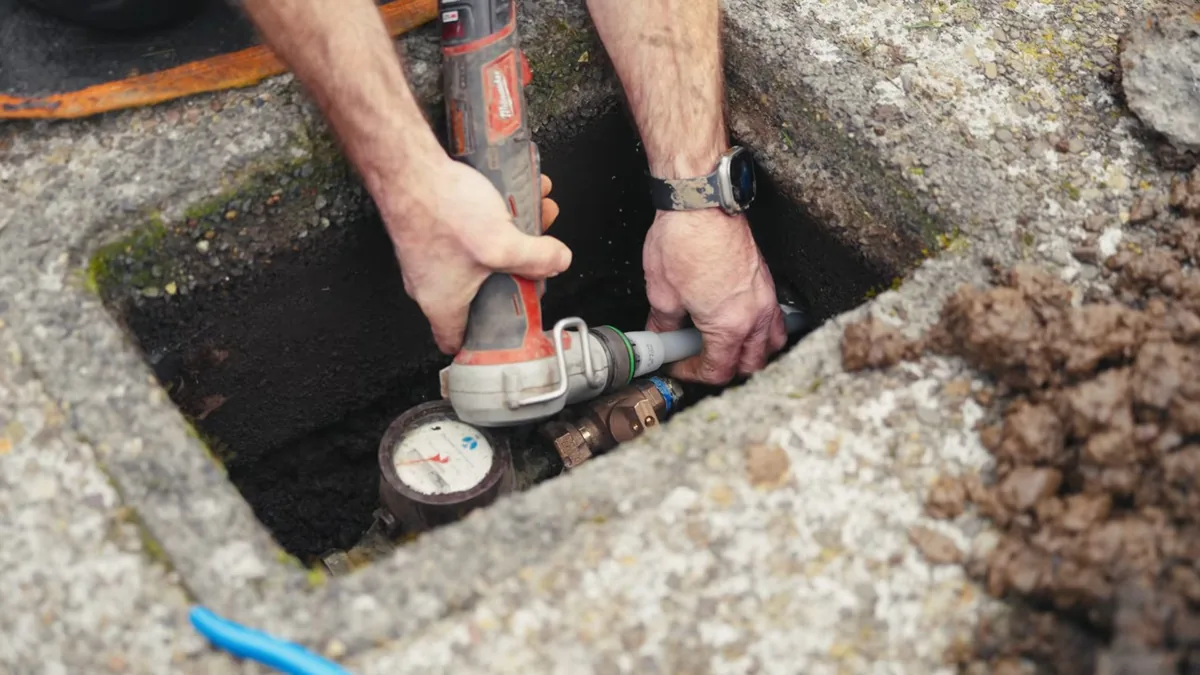 Hands using a tool on a water meter inside a concrete box in the ground