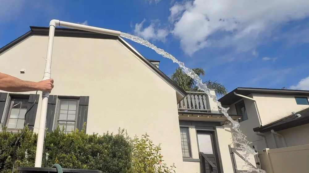 House exterior with a white pipe held up near the roofline and water spraying from the top