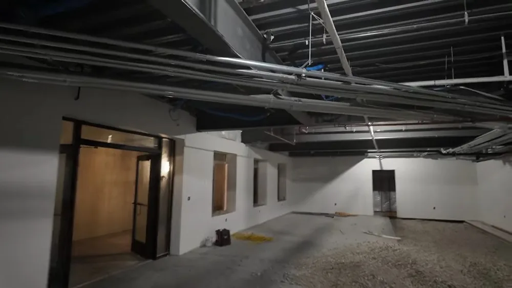 Overhead pipes and conduit running across the ceiling of an unfinished commercial space with doorways and gravel on the floor