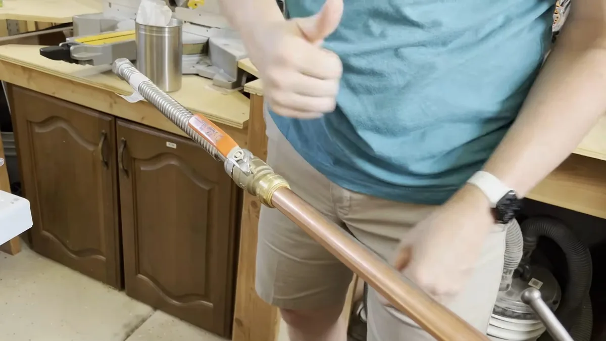 Person giving a thumbs up while holding a length of copper pipe in a kitchen with wooden cabinets