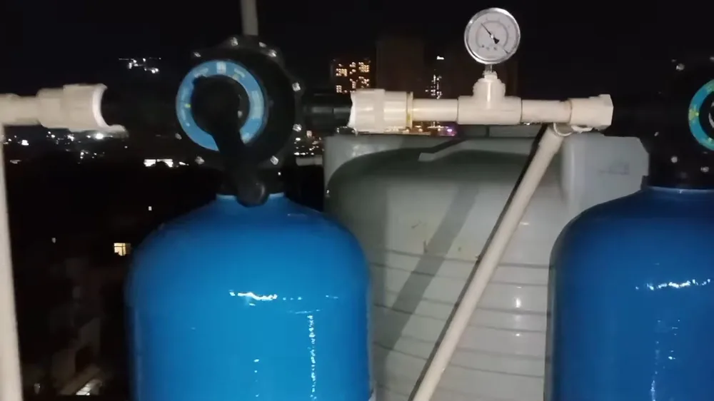 Pressure gauge on a white pipe between two blue treatment tanks, photographed at night