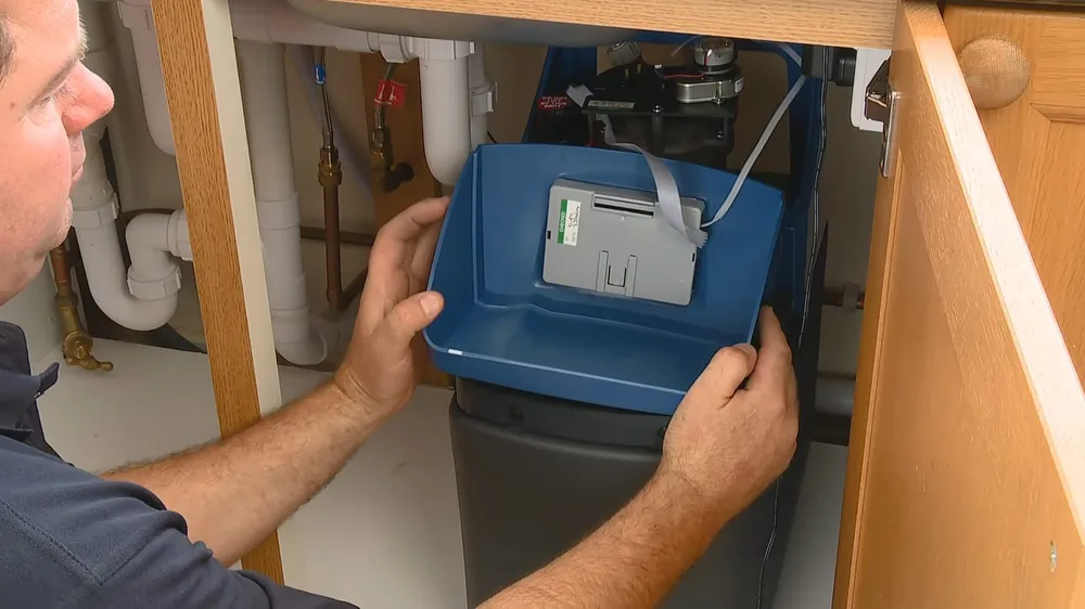 Technician setting a blue water softener unit into place beneath a kitchen sink
