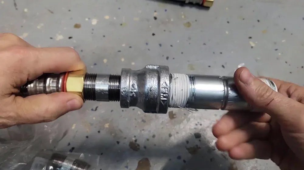 Two hands joining a metal coupling onto a pipe over a speckled workshop floor