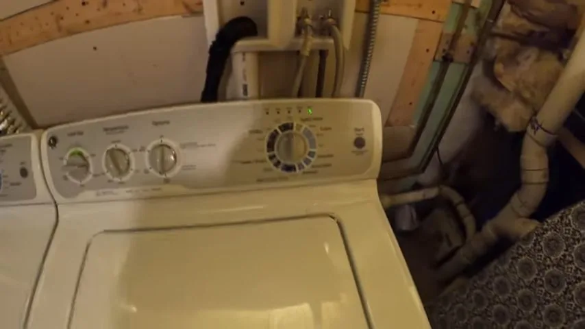 Washing machine against a basement wall with water supply lines and drain pipes running behind it