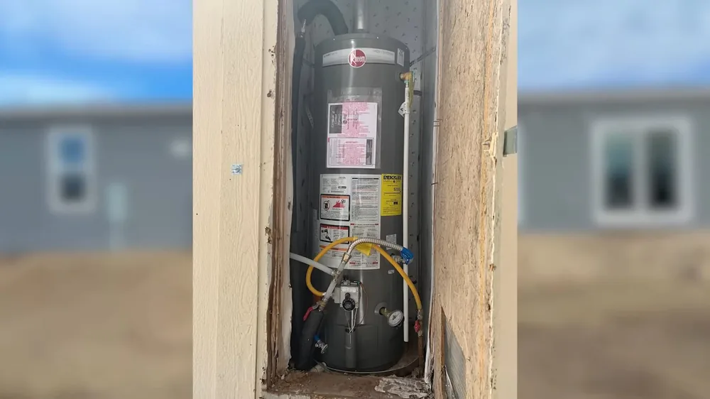 Water heater seen through a narrow wall opening, with blurred houses in the background