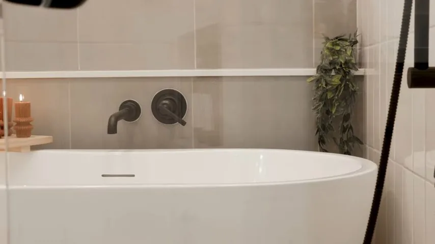 White freestanding bathtub with matte black wall-mounted fixtures and a plant on the shelf