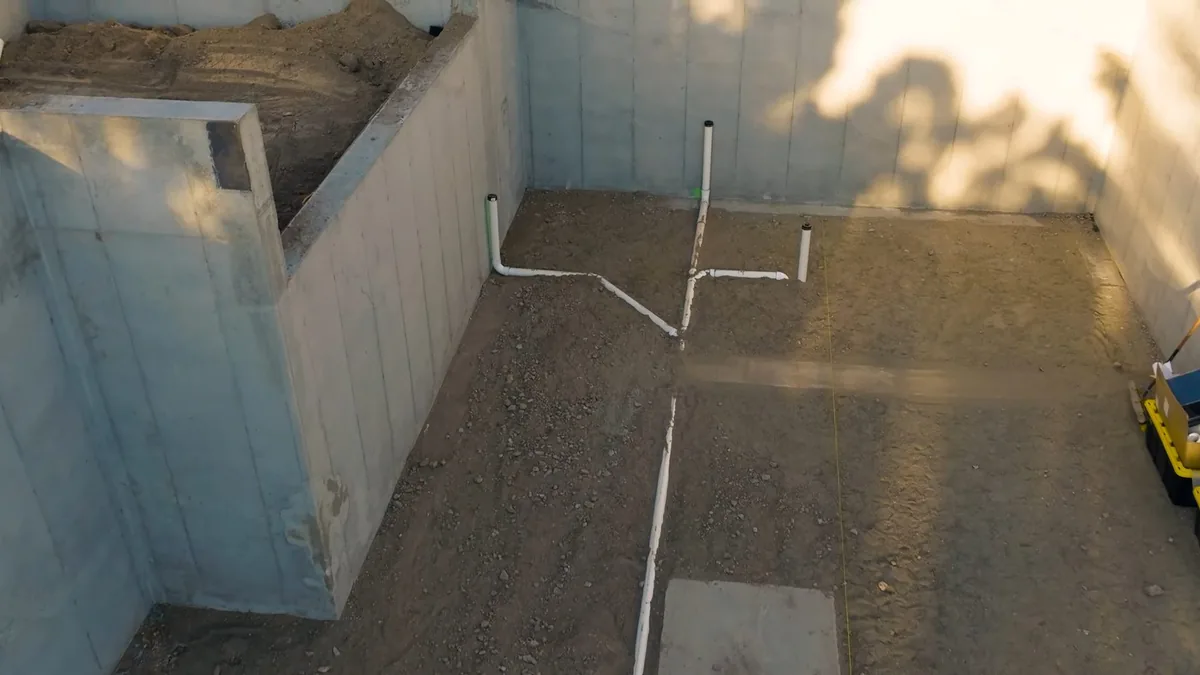 White PVC drain lines laid out in a sand-floored pit surrounded by tiled walls