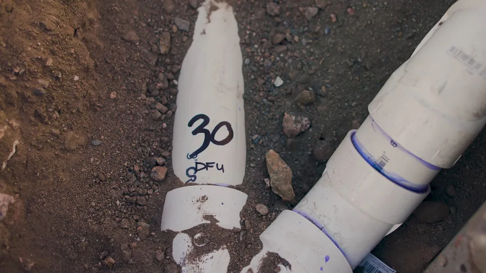 White PVC drain pipes with a flow rating written on one, laid in an excavated dirt trench