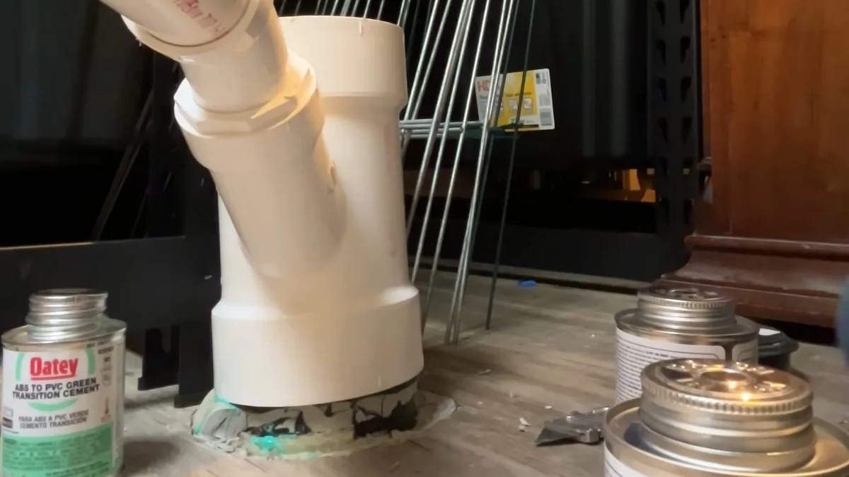White PVC tee with solvent cement cans beside it, on a workbench under a sink basin