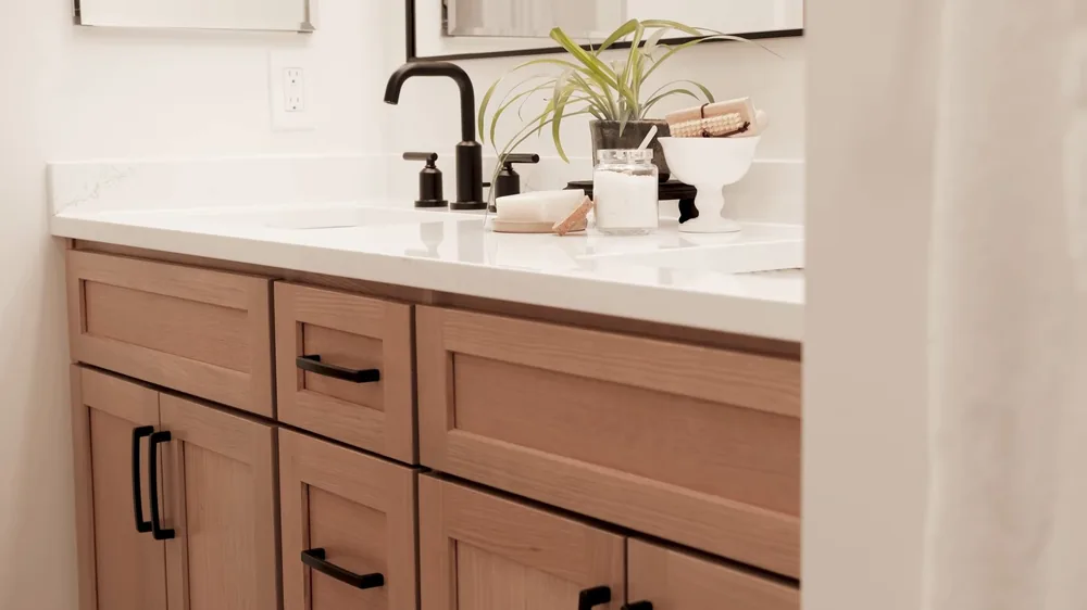 Wooden bathroom vanity with a white countertop, a black faucet and a small plant