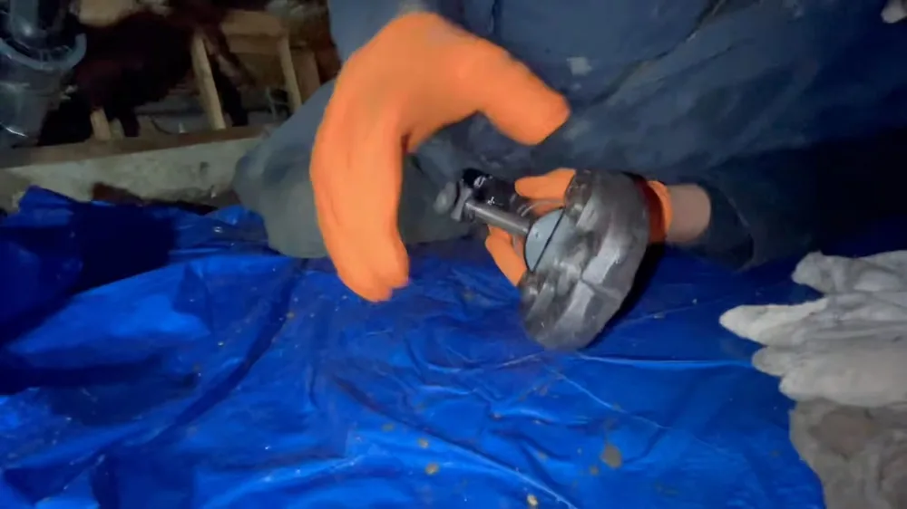 Worker in orange gloves holding a round pipe flange on a blue tarp