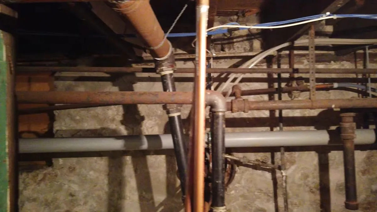 Basement ceiling with exposed water pipes and drain lines running between the joists