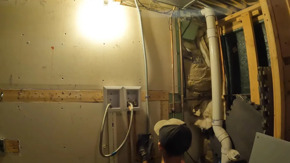 Basement laundry area with white PVC drain lines and a man in a cap bent over the framing