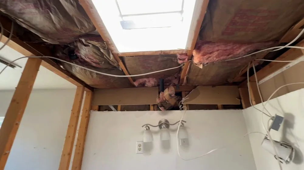 Bathroom ceiling cut open to show wooden joists and insulation, with a bright skylight above