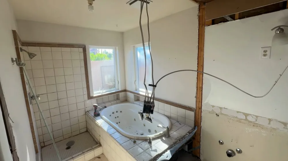 Bathroom with walls opened to the studs, a tub, tile and wires hanging from the wall