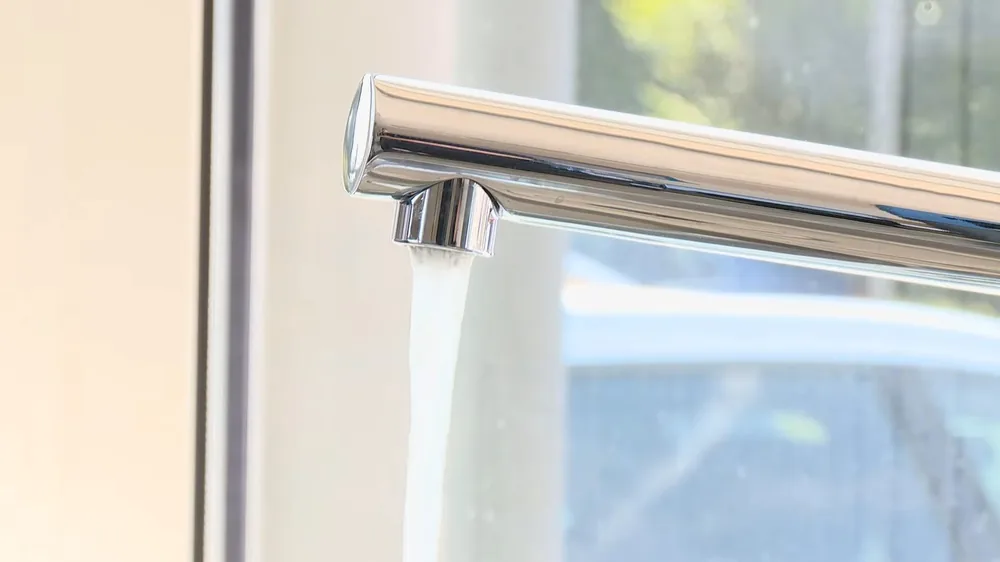 Chrome kitchen faucet with water running from the spout, beside a bright window