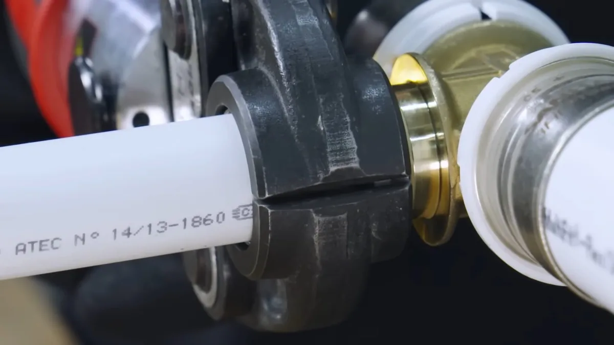 Close-up of a white PEX tube inside a black press fitting with brass parts