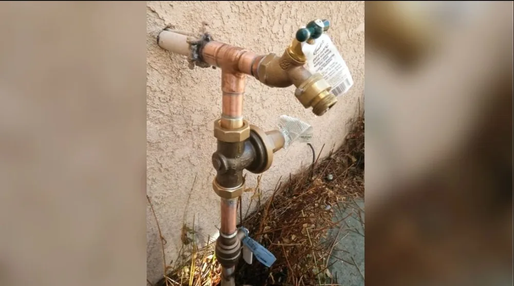 Copper shutoff valve and hose bib on a stucco wall with a paper tag attached, and dry brush at the base