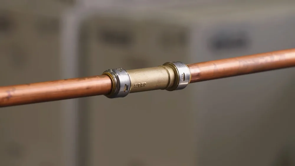 Copper water pipe joined by a brass coupling, with a softly blurred room behind it