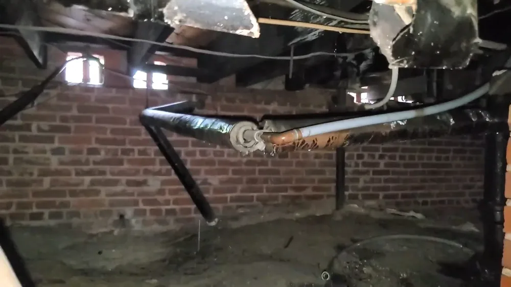 Crawl space with a black pipe and a white line running along a brick foundation wall