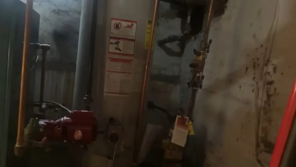 Dim utility room with a water heater, a red circulating pump and copper and gas lines running along the wall