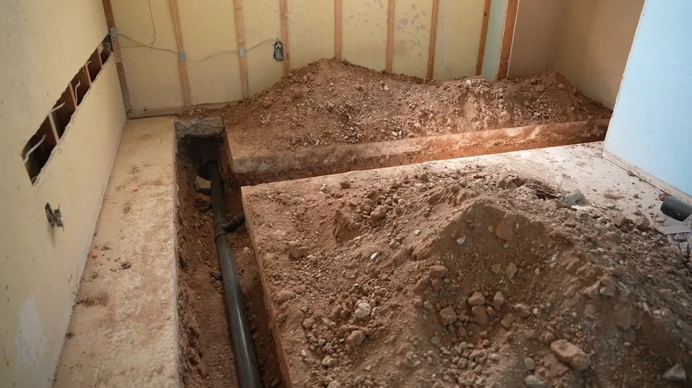 Excavated trench of loose soil inside a room with exposed wall studs
