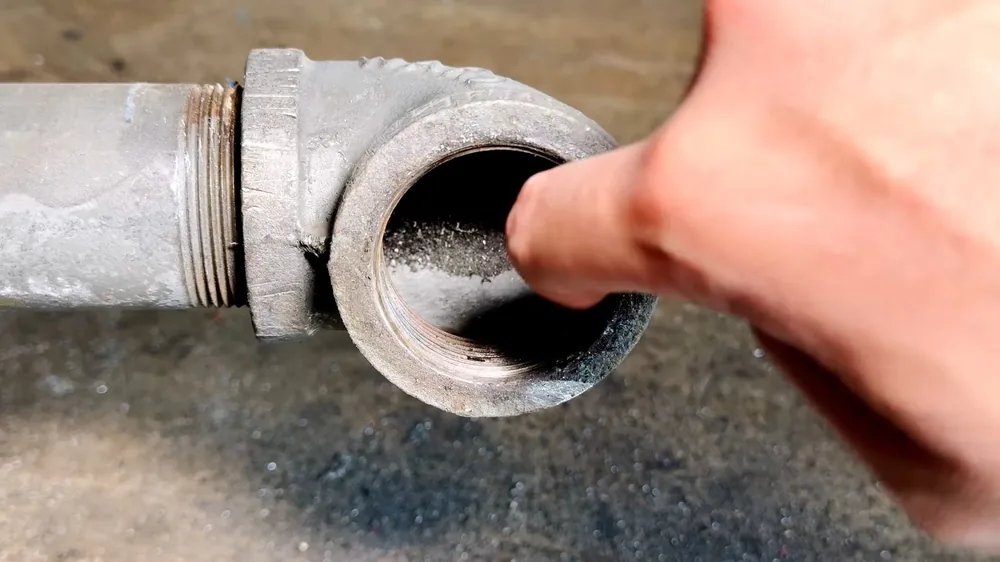 Finger resting at the open threaded end of a galvanized cleanout fitting