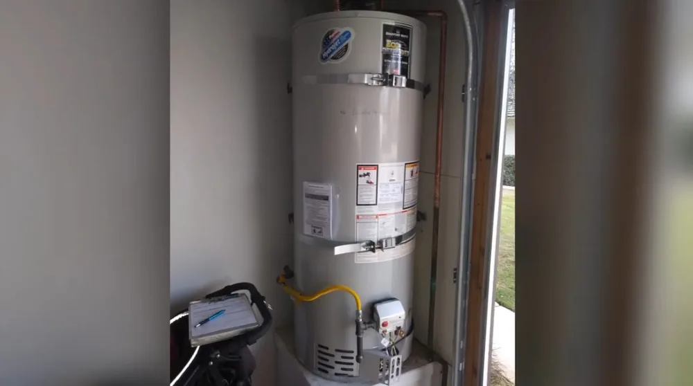 Gas tank water heater standing in a narrow closet with a drain pan and a wall panel beside it