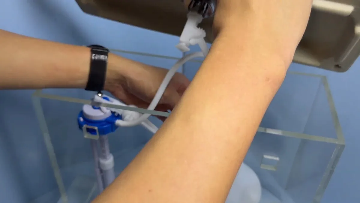 Hand adjusting the fill valve inside a clear demonstration toilet tank