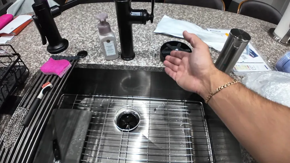 Hand gesturing over a stainless steel kitchen sink with a mesh strainer and a modern faucet