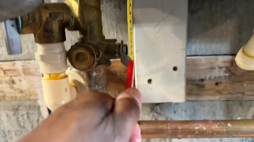 Hand holding a tape measure beside a brass service valve and white pipes at a tankless unit