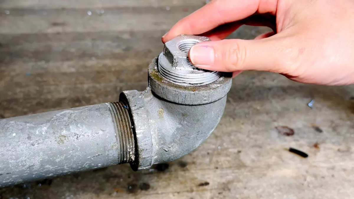 Hand unscrewing a threaded cap from the cleanout elbow on a galvanized pipe