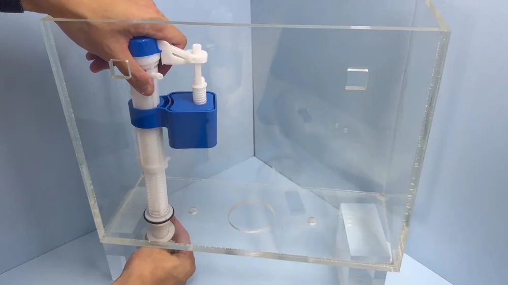 Hands holding a flush and fill valve kit inside a clear toilet tank model