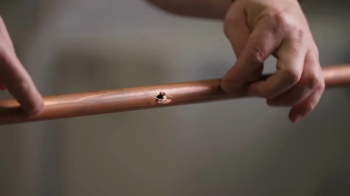 Hands holding a length of copper pipe that has a small pinhole leak in its wall