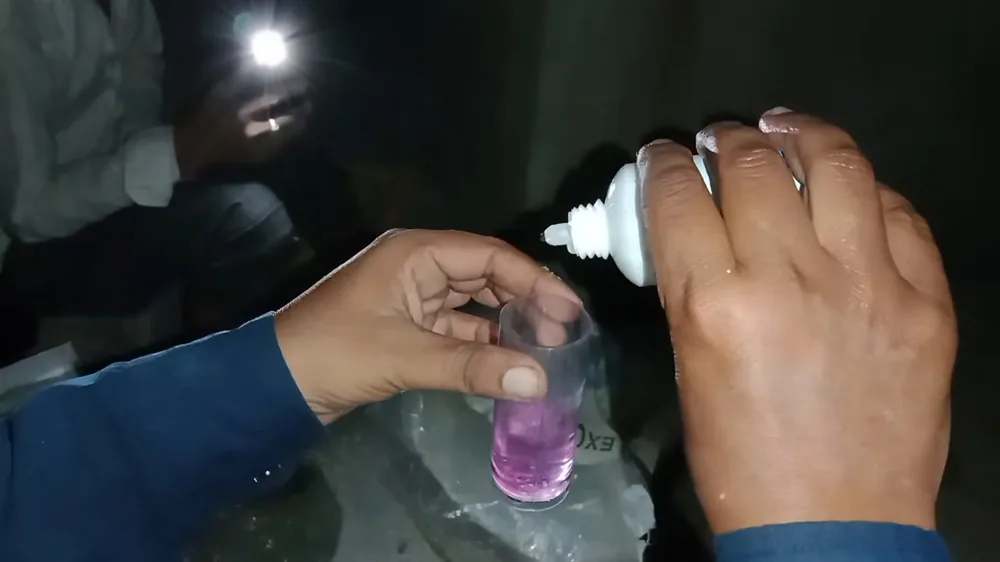 Hands holding a small test cup with a purple liquid while another hand squeezes drops from a white bottle