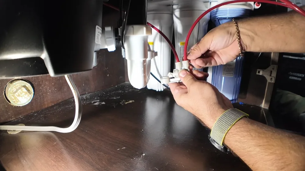 Hands joining two wire connectors beside an under-sink unit, with a red wire and a filter housing in view