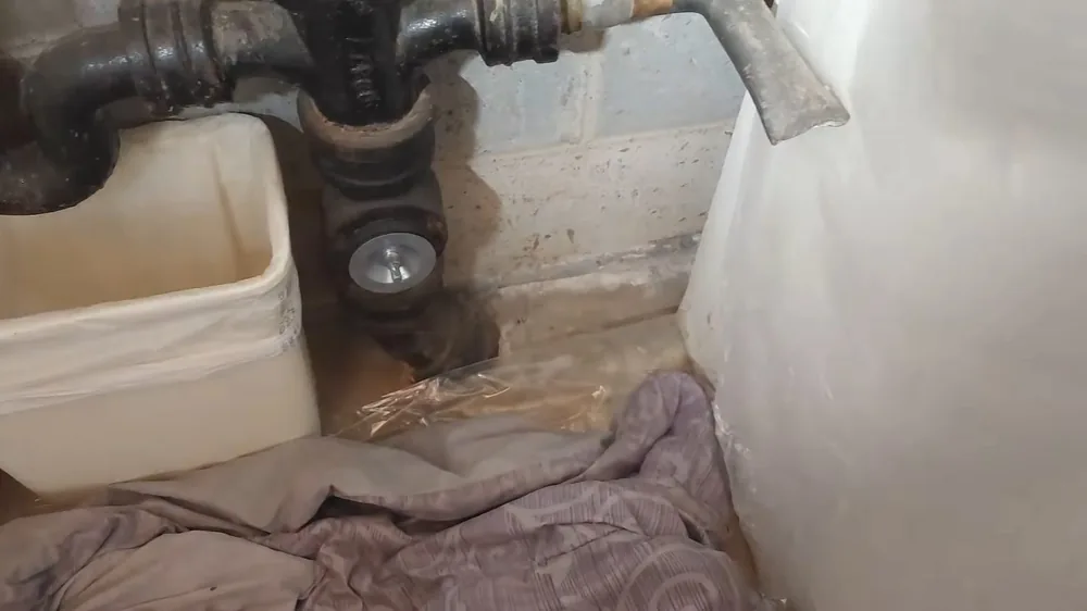 Old cast iron drain pipes in an opening cut into a concrete bathroom floor, with a plastic-covered tub beside it