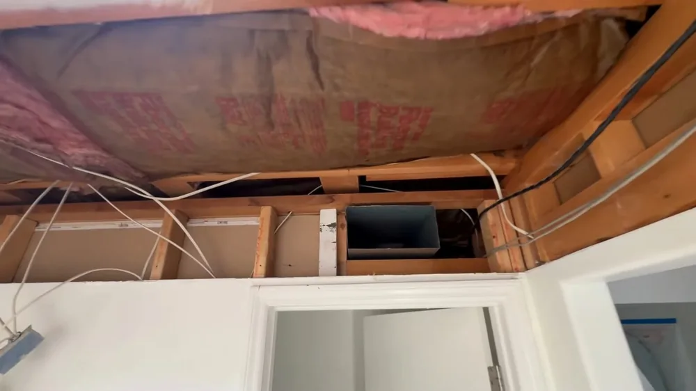 Opened ceiling with pink insulation and joists above a doorway in a stripped room