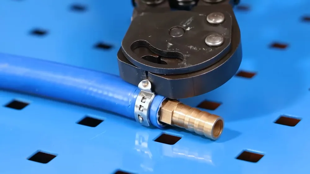 Press tool crimping a blue PEX tube onto a brass fitting on a blue pegboard